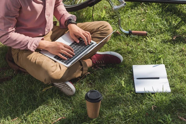 Freelancer laptop kahve ve park içinde defter ile yeşil çimenlerin üzerinde çalışan kısmi görünümü