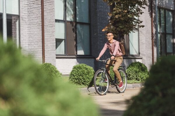  asian young man with backpack riding bicycle on street