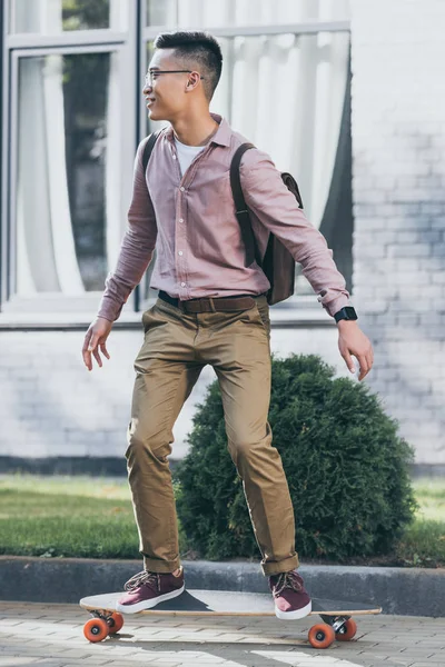 Junger Asiatischer Mann Mit Rucksack Reitet Longboard Auf Straße — kostenloses Stockfoto