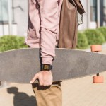 Partial view of man with backpack holding longboard on street