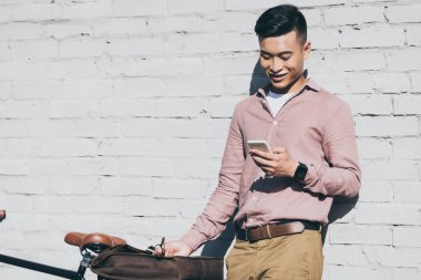 Sokakta duran Bisiklet yakınındaki Smartphone kullanarak gülümseyen Asyalı adam