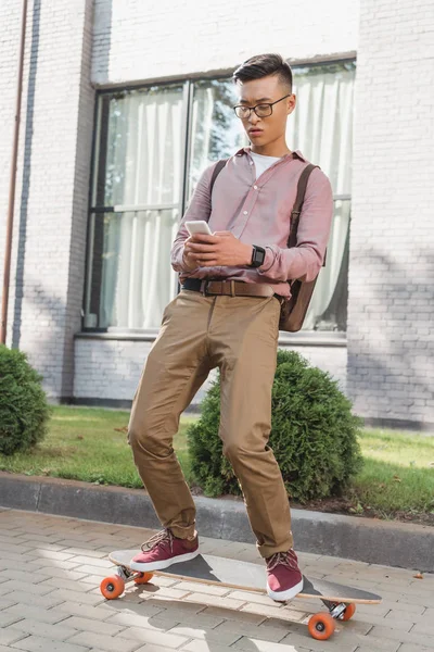 Fokussierter Asiatischer Mann Benutzt Smartphone Während Auf Dem Longboard Auf — Stockfoto