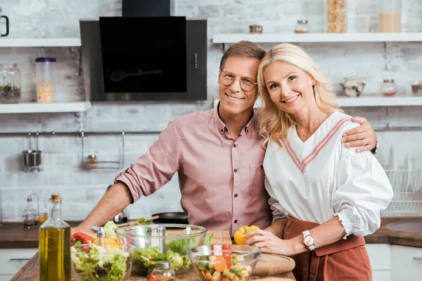 Affectionate Adult Couple Hugging Looking Camera Salad Preparation Dinner Kitchen — Stock Photo, Image