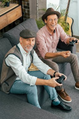 happy mature men playing with joysticks and smiling at camera, high angle view clipart