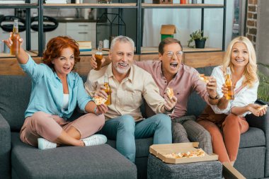 excited mature friends drinking beer and eating pizza at home clipart