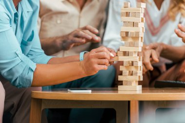 cropped shot of mature friends building tower from wooden blocks on table