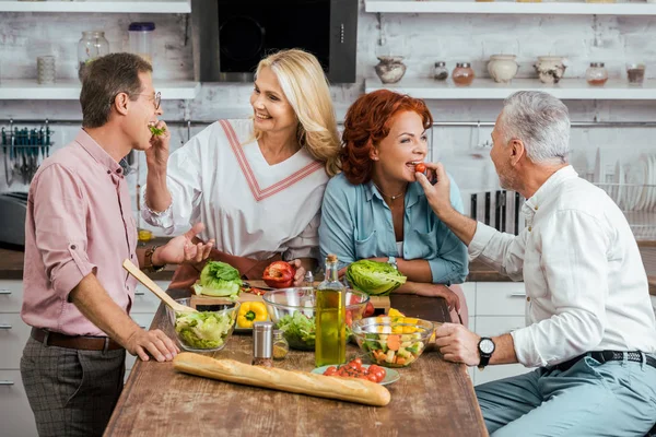 Felizes Casais Maduros Alimentando Uns Aos Outros Durante Preparação Salada — Fotografia de Stock