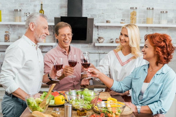 smiling old friends clinking with wineglasses in kitchen
