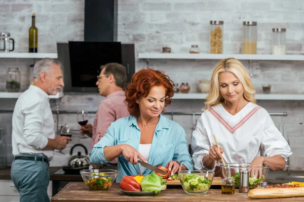 Sonrientes Mujeres Atractivas Preparando Ensalada Para Cena Hombres Hablando Con — Foto de stock gratis