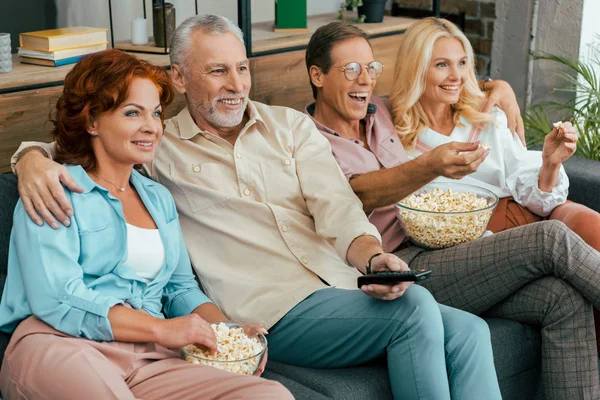 happy old friends eating popcorn and watching tv together