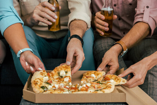 cropped shot of mature friends drinking beer and eating pizza together