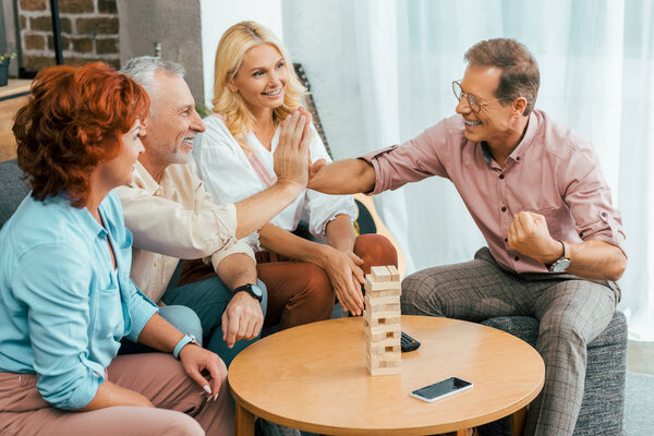 happy mature men giving high five while playing with wooden blocks at home
