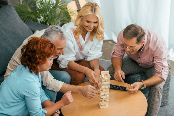 high angle view of smiling old friends building tower from wooden blocks on table