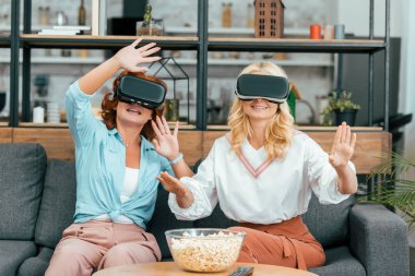 smiling mature female friends using virtual reality headsets at home