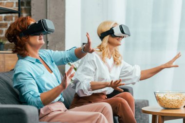 happy mature women sitting on couch and using virtual reality headsets 