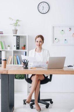 gülümseyen iş kadını işyerinde modern Office belgeleri ve dizüstü bilgisayar ile çalışma