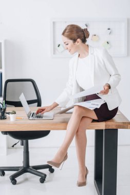 işkadını modern ofiste tabloda otururken belgeleri ve dizüstü bilgisayar ile çalışma