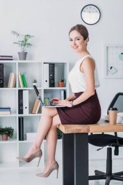 gülümseyen Yöneticisi ofiste tabloda otururken dizüstü bilgisayar ile çalışma