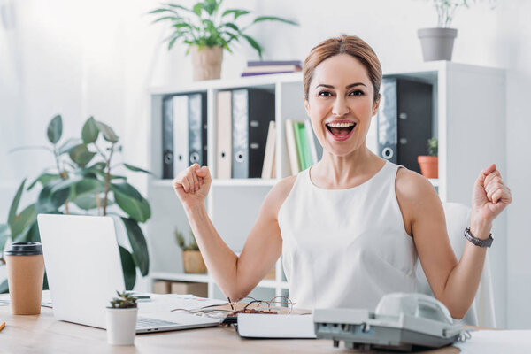 beautiful excited businesswoman celebrating success at workplace with laptop