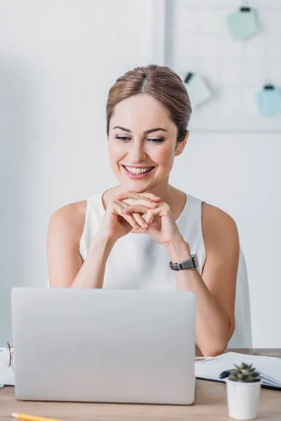 職場で座ってノート パソコンの画面を見て美しい幸せな実業家 — ストック写真