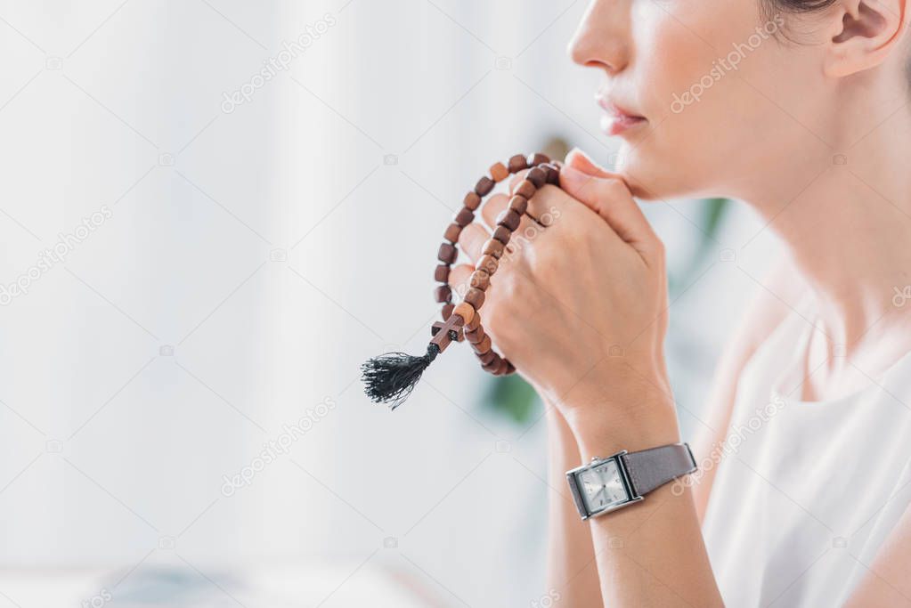 cropped view of woman praying with wooden rosary beads