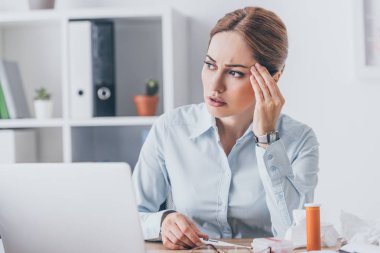 İşyerinde oturan ve uzağa bakarken elektrik termometre tutan hastalıklı işkadını