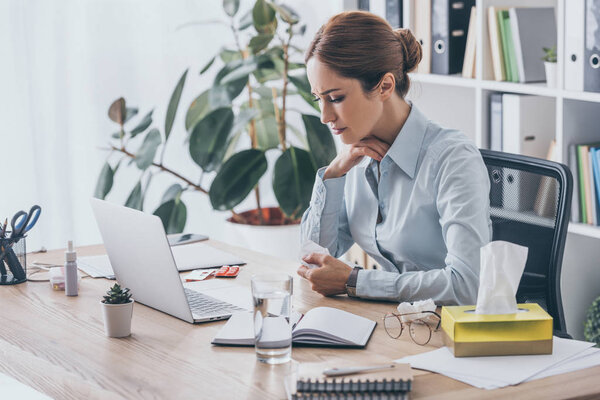 adult sick businesswoman with sore throat trying to work at office