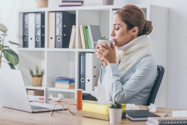 close-up portrait of ill businesswoman in scarf drinking hot tea at office