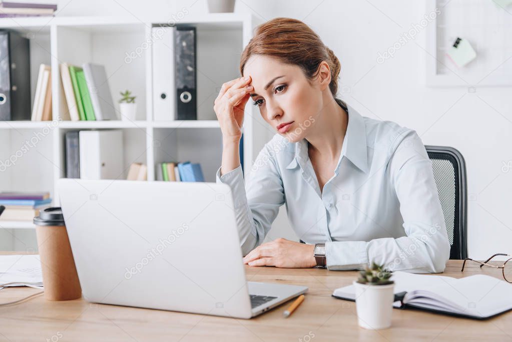 exhausted adult businesswoman with headache touching her head while sitting at office