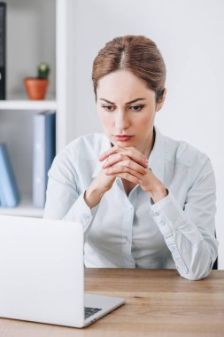 İşyerinde oturan ve dizüstü bilgisayar ekranına bakarak ciddi iş kadını