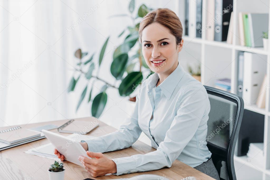 smiling beautiful businesswoman working with tablet at office and looking at camera