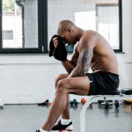 Widok z boku mięśni młody sportowiec ocierając czoło ręcznikiem siedząc po treningu w siłowni