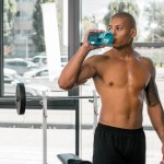 Muscular de peito nu desportista beber água e olhando para longe no ginásio