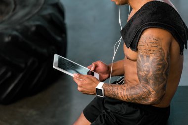 Kas dövmeli sporcu spor salonunda dijital tablet kullanarak atış kırpılmış