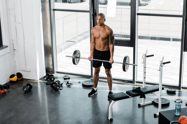 высокий угол обзора мускулистого молодого татуированного спортсмена, поднимающего штангу в спортзале
