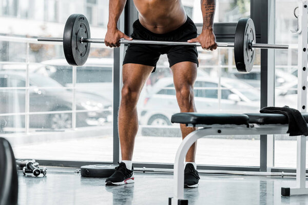 cropped shot of young athletic man lifting barbell in gym