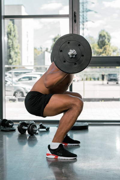 side view of young athletic man lifting barbell in gym