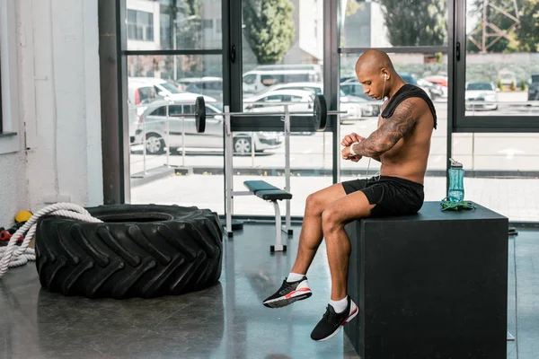 Muscular Shirtless African American Sportsman Earphone Sitting Using Smartwatch Gym — Stok Foto