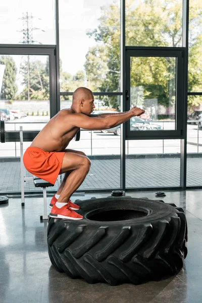 Vista Lateral Del Atleta Afroamericano Haciendo Sentadillas Neumático Gimnasio — Foto de Stock