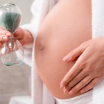 Przycięty Zrzut z kobieta w ciąży, trzymając klepsydry w pobliżu brzuch w łazience