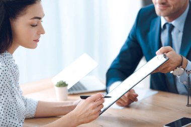 cropped shot of lawyer holding clipboard and young woman signing document  clipart