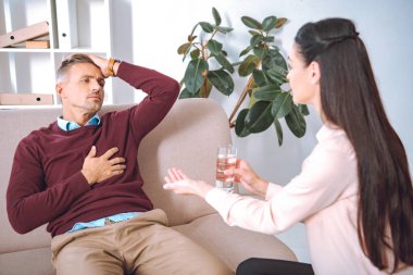 psychotherapist giving glass of water and pill to patient with heartache  clipart