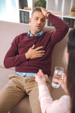 cropped shot of psychotherapist giving glass of water and pill to stressed patient with heartache  clipart