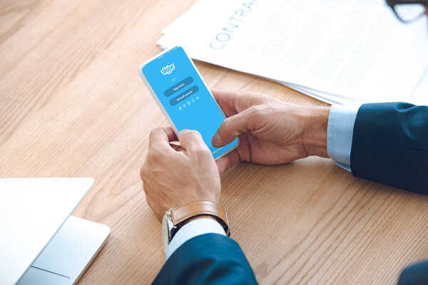 обрезанный снимок бизнесмена с помощью смартфона с приложением skype на экране
