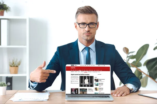 英俊的商人在眼镜指向笔记本电脑与 Bbc 新闻网站在屏幕上 — 图库照片
