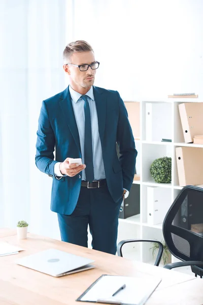 Confident Businessman Eyeglasses Holding Smartphone Looking Away Office — Stock Photo, Image