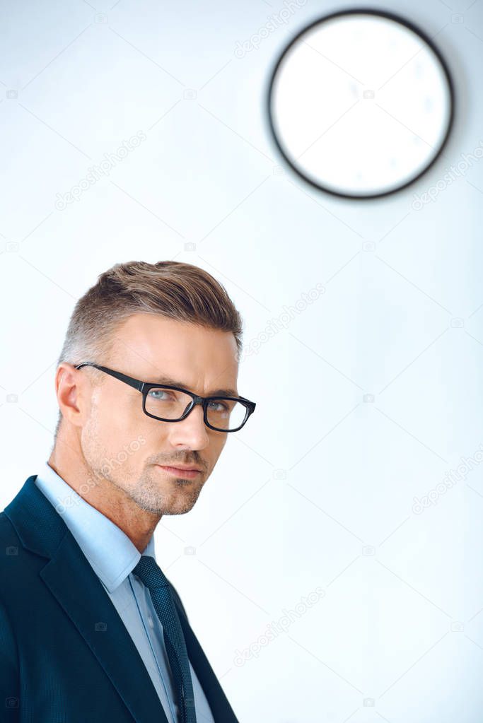handsome businessman in eyeglasses and formal wear looking at camera