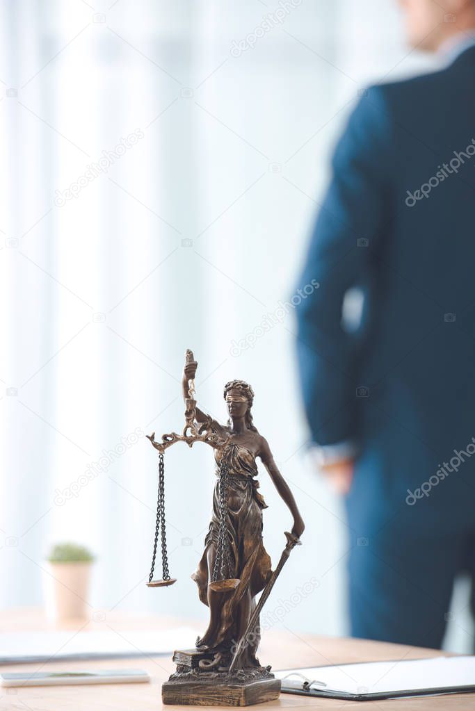 close-up view of lady justice statue and lawyer standing behind 