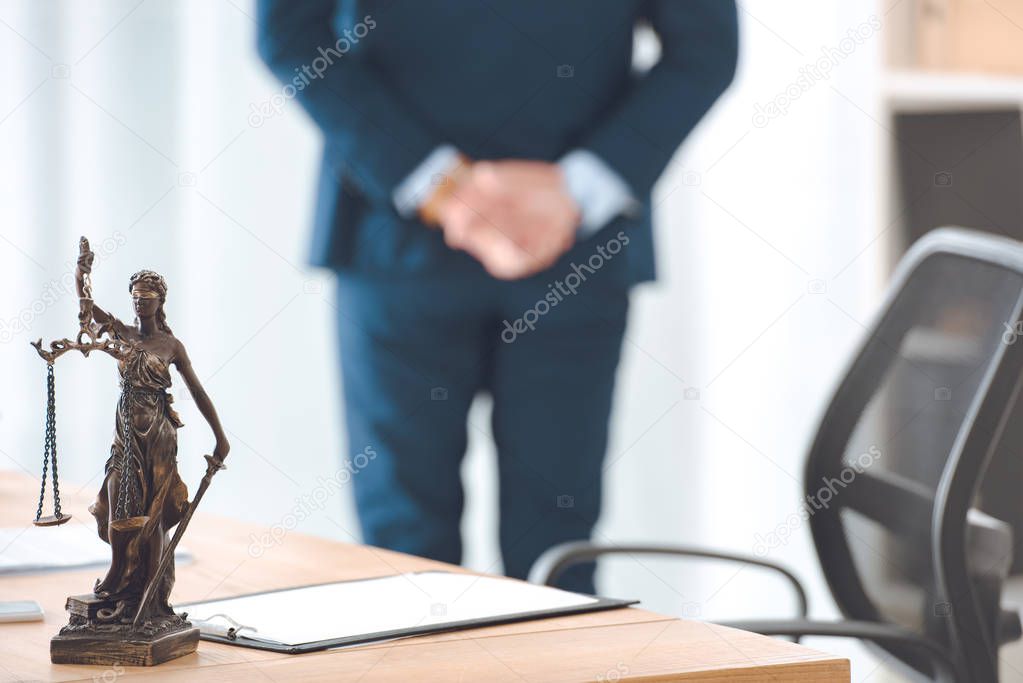 close-up view of lady justice statue and clipboard on table and lawyer standing behind 