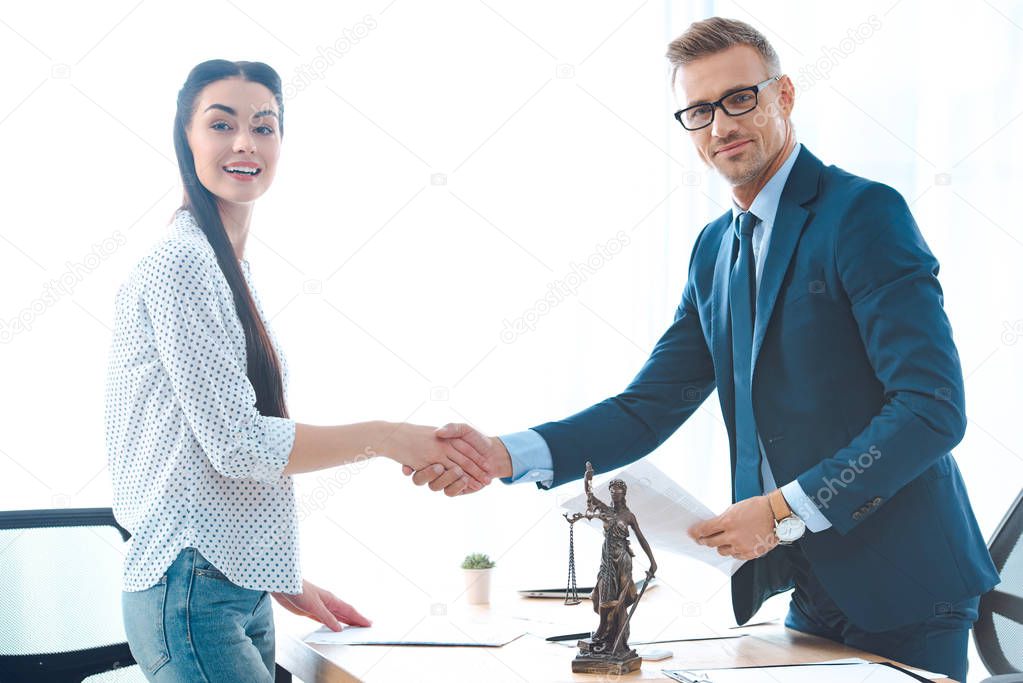 professional lawyer and young female client shaking hands and smiling at camera